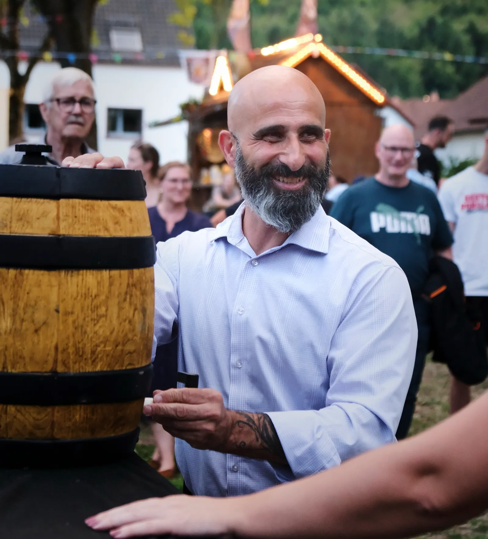 Nader Samadi Tehrani im hellblauen Hemd an einem hölzernen Fass, eine Hand auf dem Fassdeckel, in der anderen der Zapfhahn