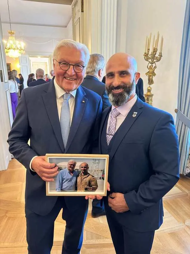 Bundespräsident Frank-Walter Steinmeier und Nader Samadi Tehrani stehen in einem Saal des Schlosses Bellevue und halten gemeinsam ein gerahmtes Foto